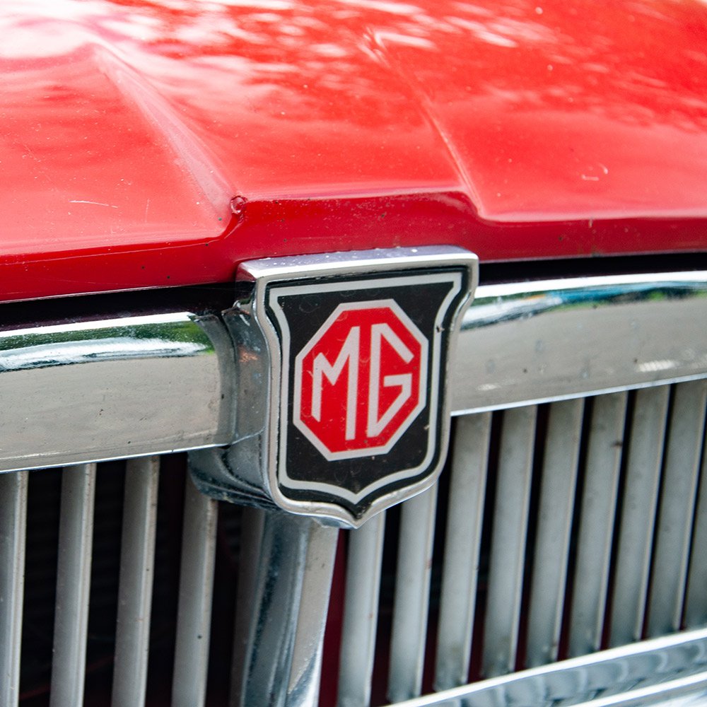 Close-up of the front grille of a vintage red MG car, featuring the MG logo badge.