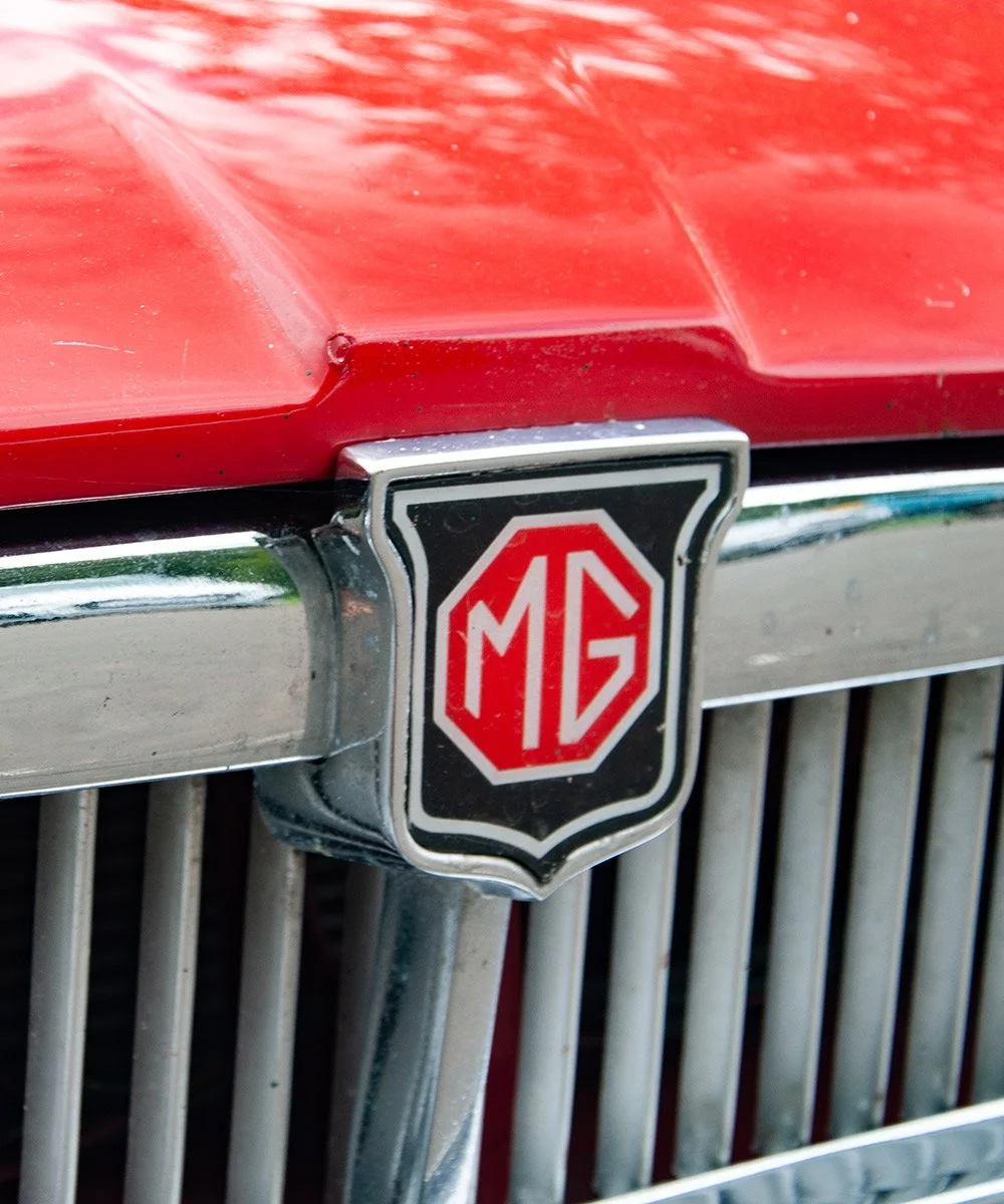Close-up of the front grille of a classic red MG car, showing the MG emblem badge.