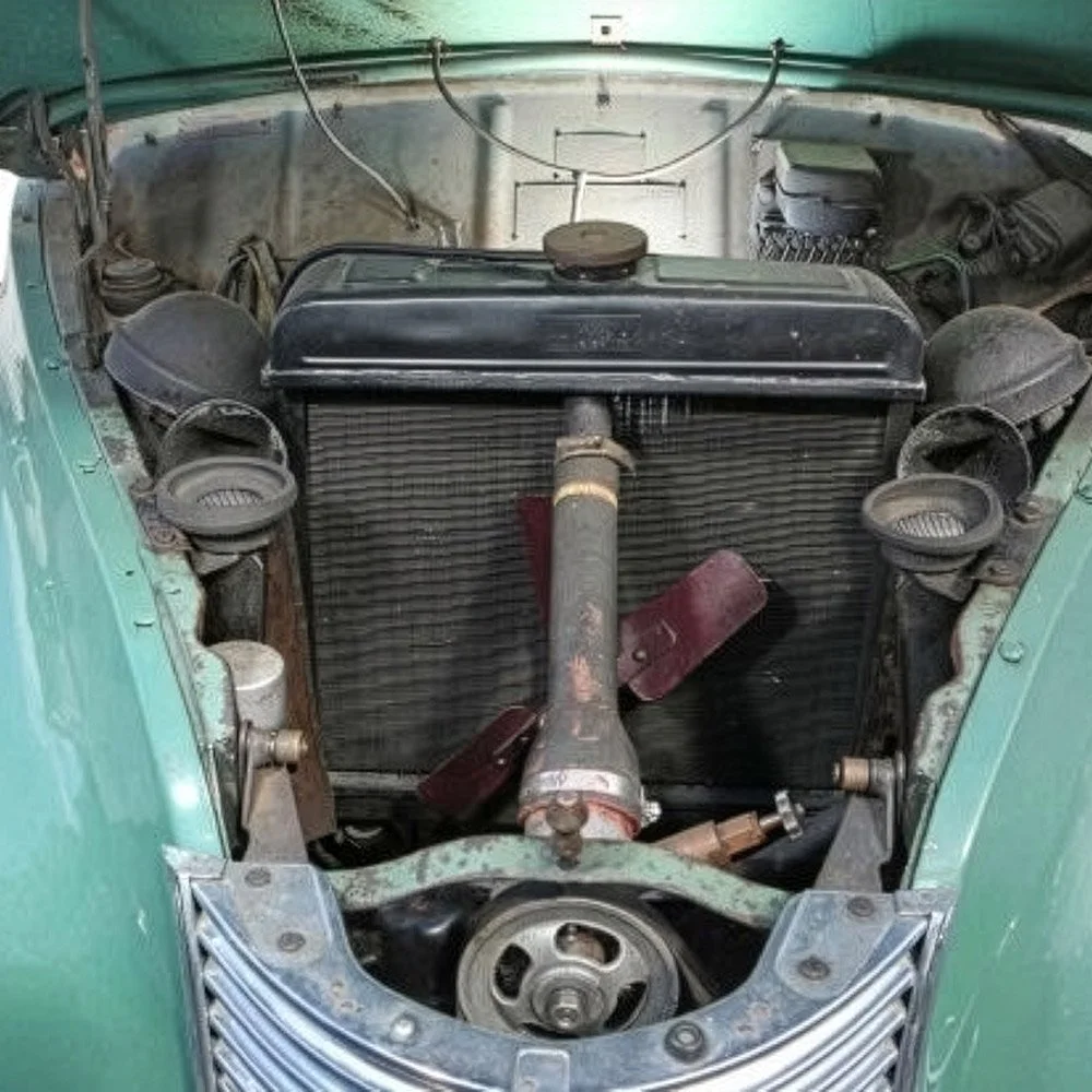 Engine bay of a vintage green car with the radiator and fan assembly visible.