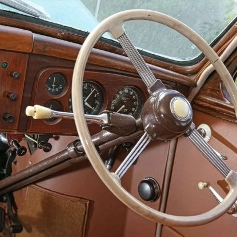 Close-up of a vintage car dashboard with a large steering wheel, speedometer, fuel gauge, and other controls on a wooden panel.