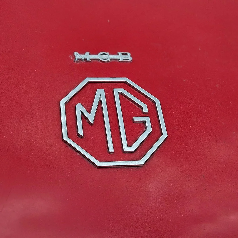 Close-up of a red surface with a silver MG logo and the letters MGB above it.