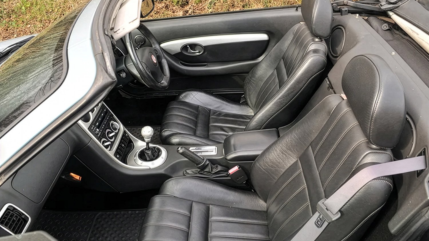 Interior of a convertible car showing black leather seats, a manual gear shift, and a dashboard with various controls.