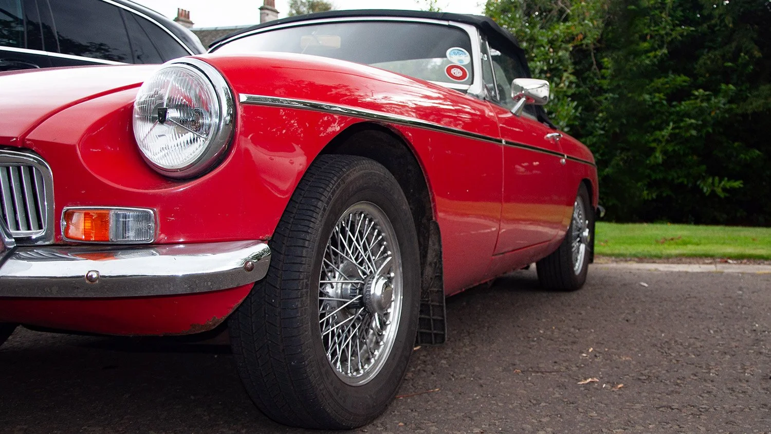 Red vintage convertible car parked on pavement with trees and grass in the background.