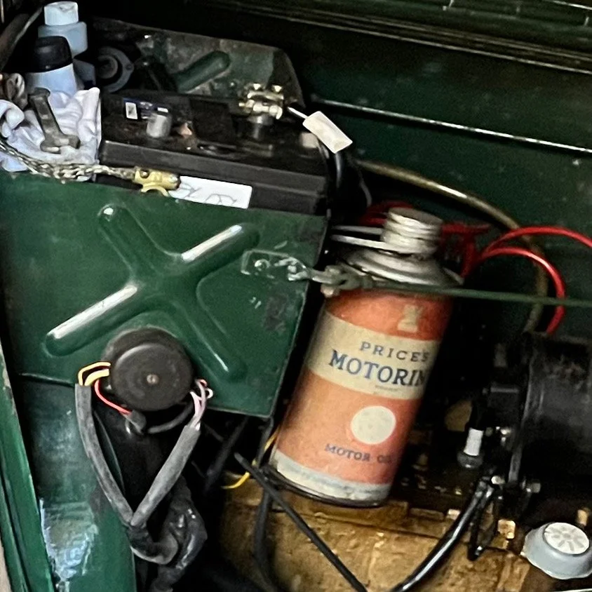 Close-up of a vintage car engine compartment showing a large green metal cover, wires, and an orange motor oil container.