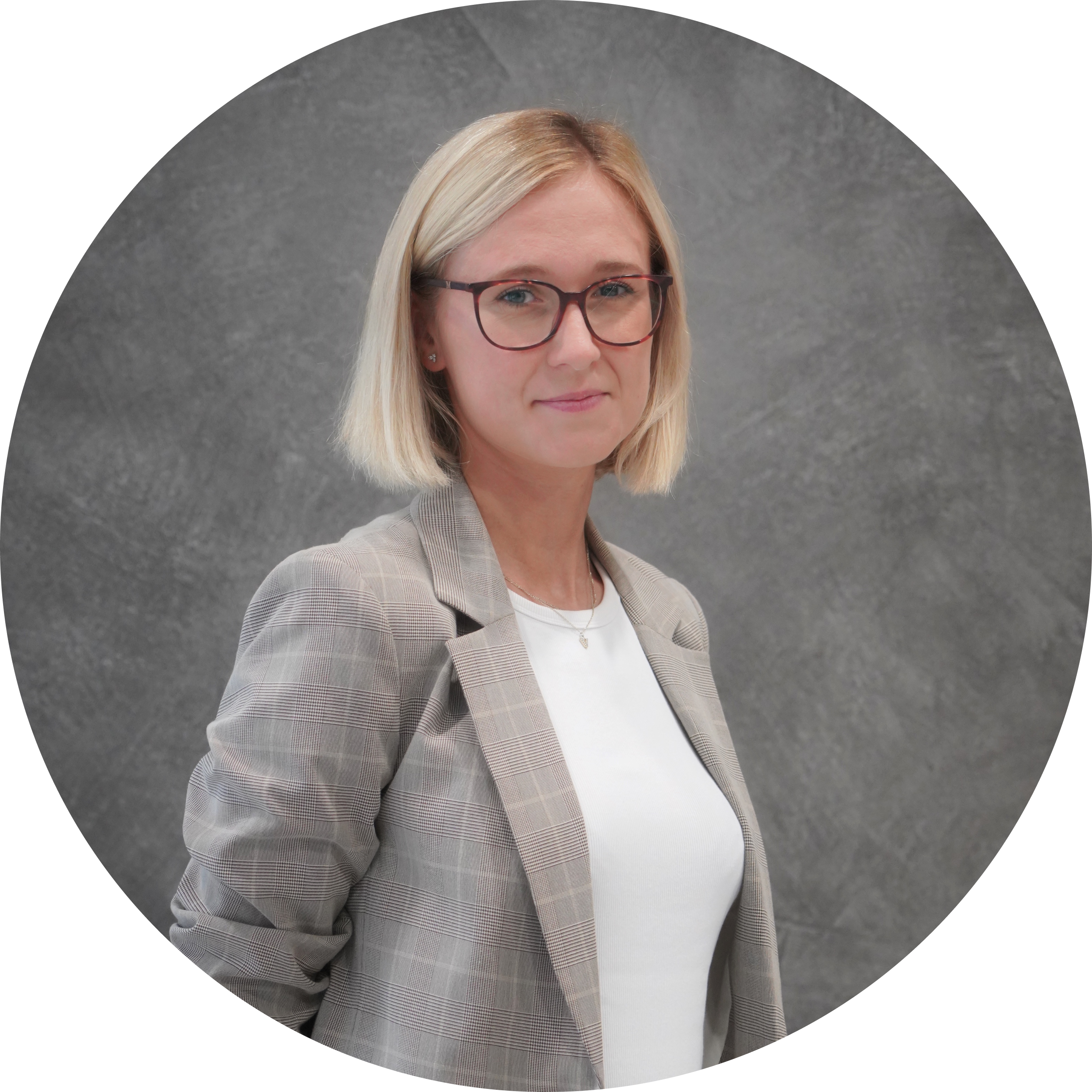 A woman with blonde, shoulder-length hair and glasses wearing a gray checkered blazer and white top, standing against a gray textured background.
