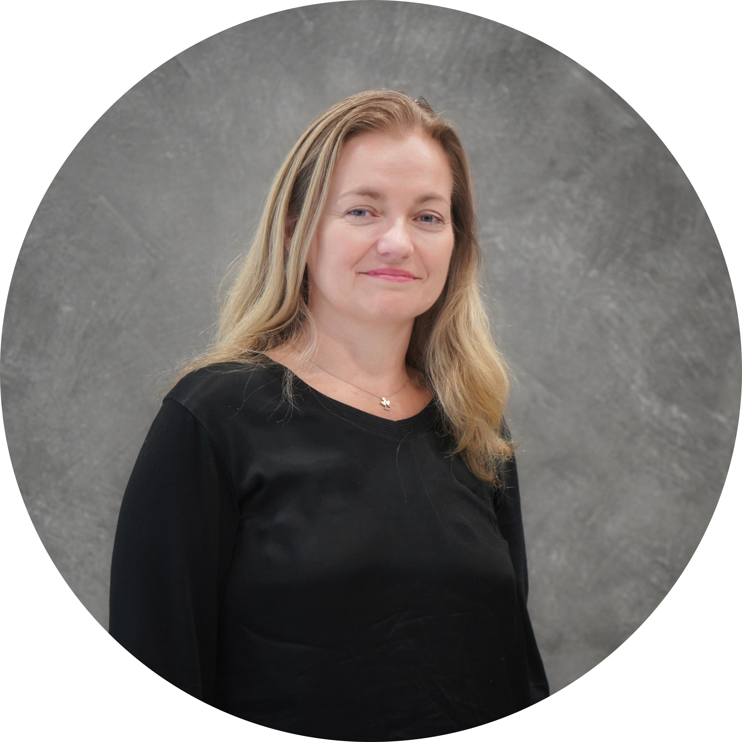 A woman with long blonde hair wearing a black top standing in front of a gray textured wall.