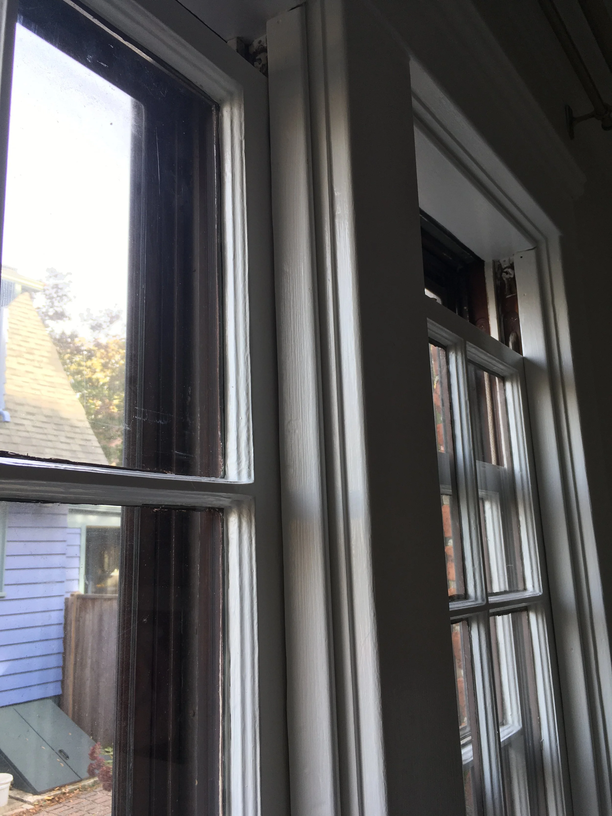 Close-up of a double-hung window with a white frame, showing the top and bottom sash, with neighboring buildings visible outside.