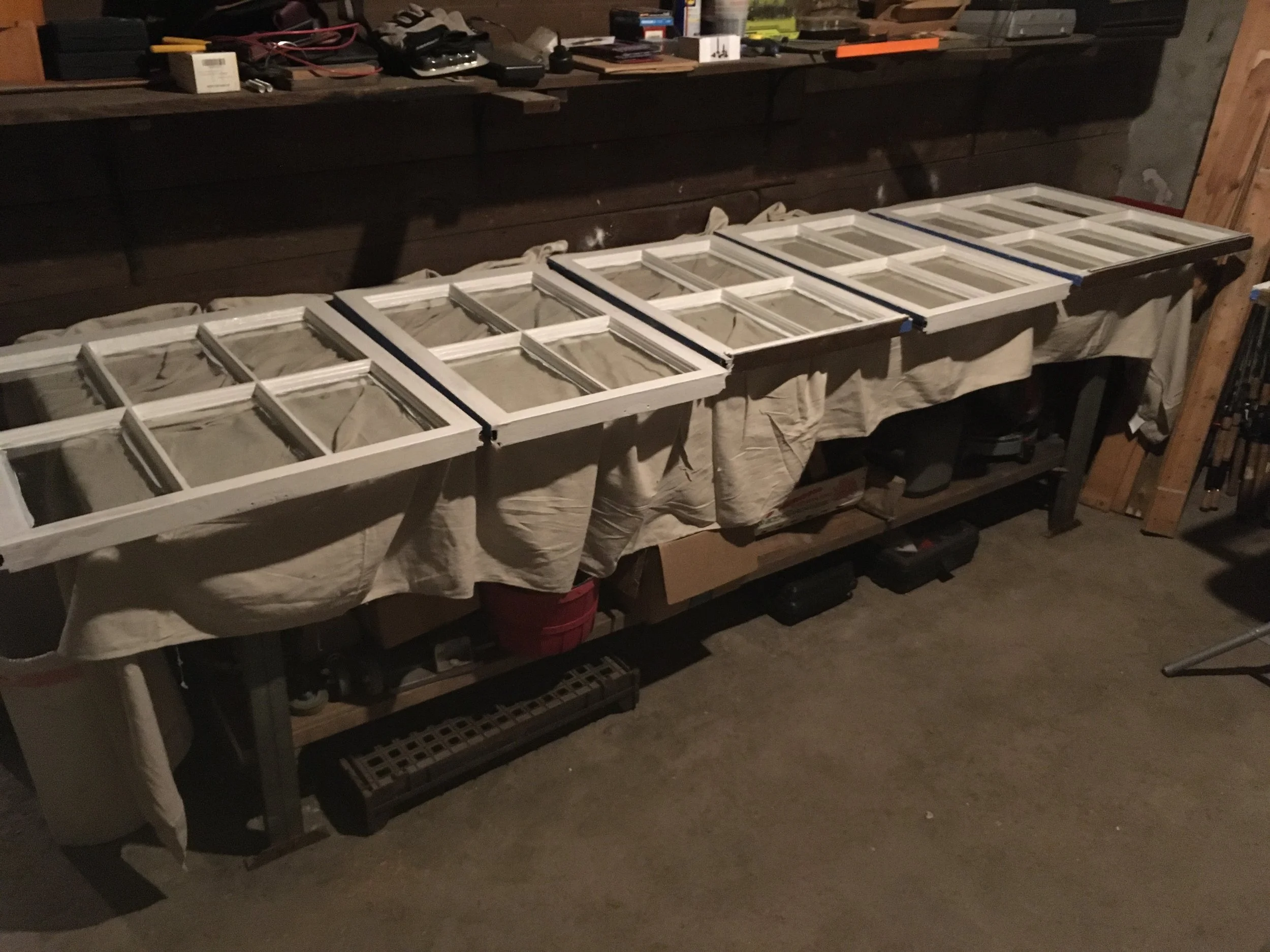 Multiple window screens laid out on a long table in a workshop or garage.