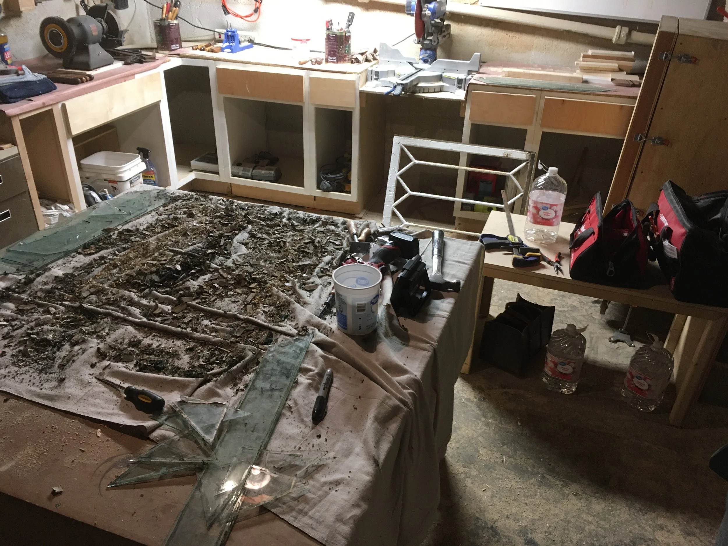 Workshop with workbenches, tools, construction supplies, and a shattered glass piece on a table.