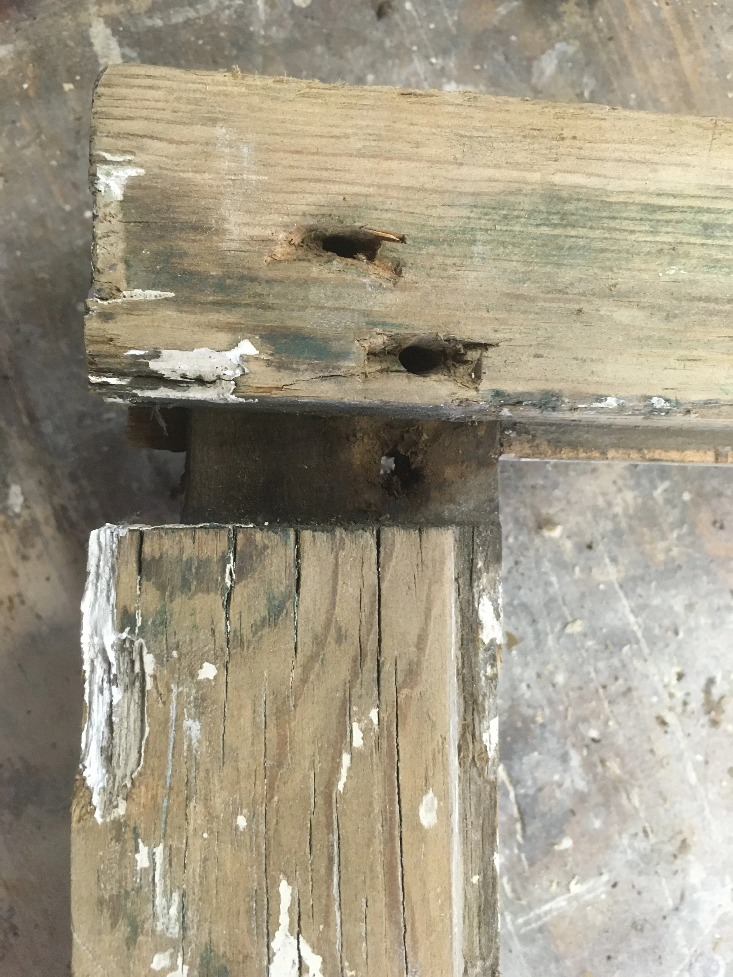 Close-up of two pieces of old, weathered wood connected with screws, showing drilled holes and chipped paint.
