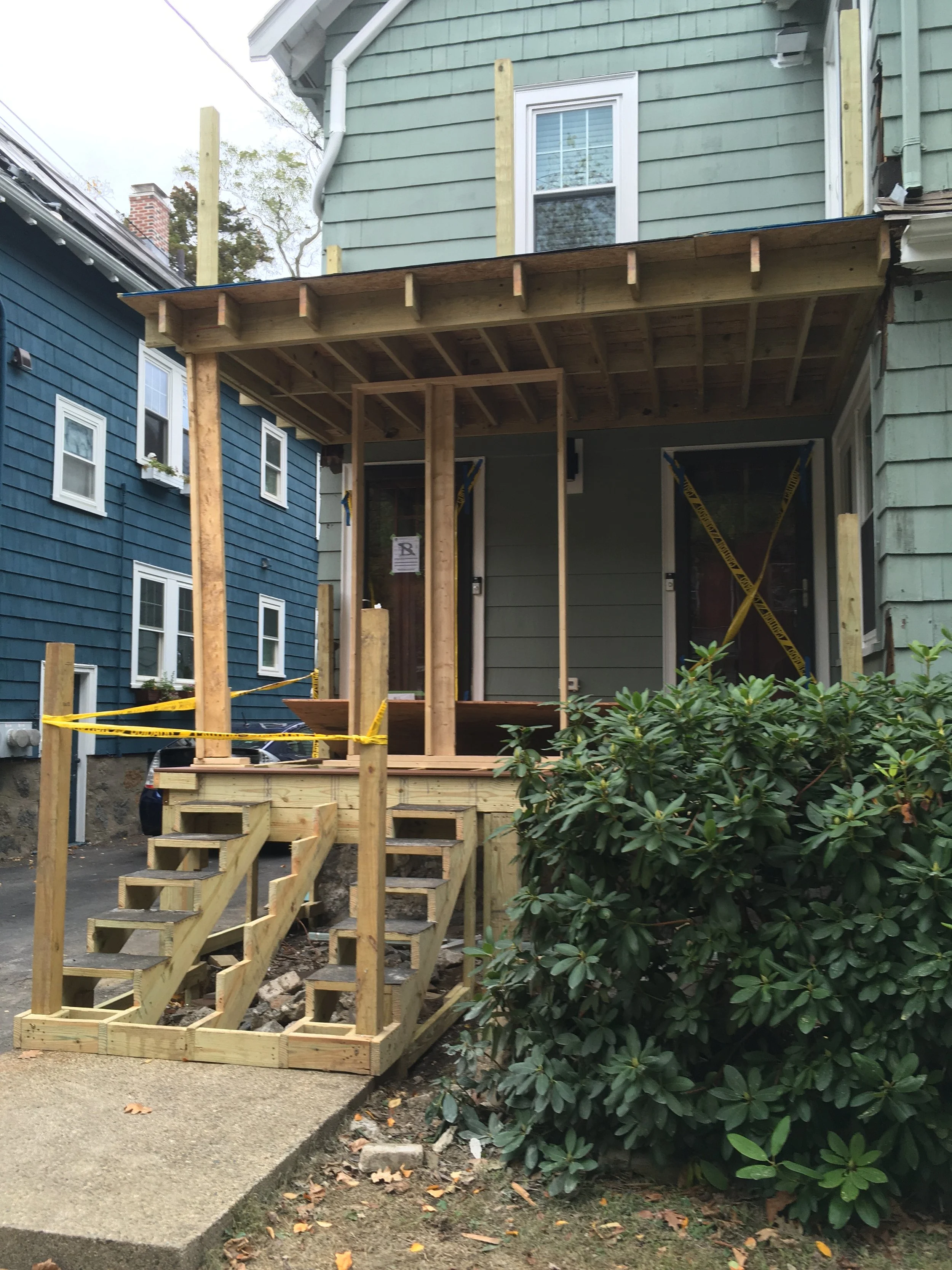 House with wooden construction on the front porch, blue wall to the left, green wall to the right, stairs leading up to the porch, and yellow caution tape.