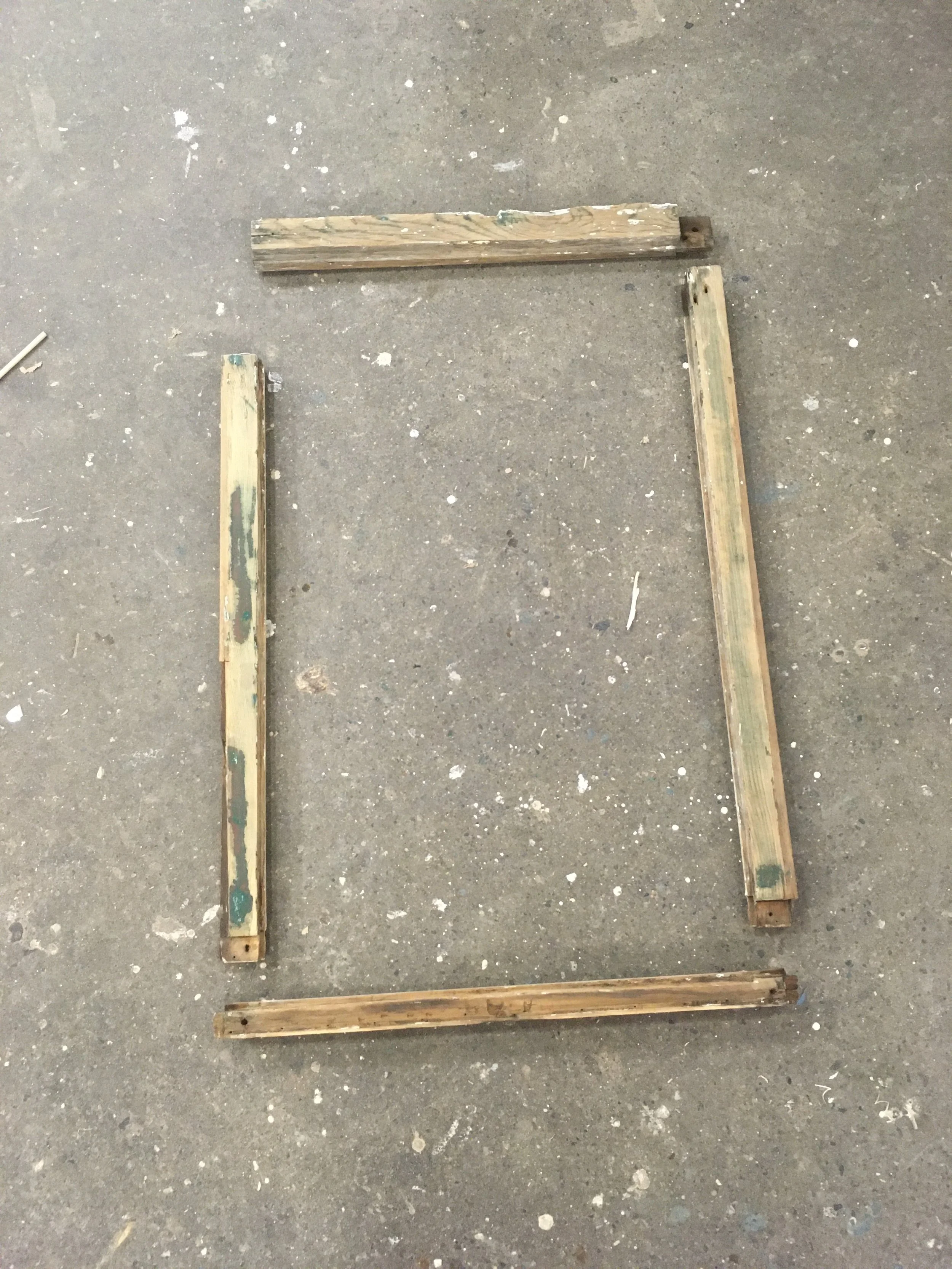 Four wooden planks arranged on a concrete floor to form a square outline.