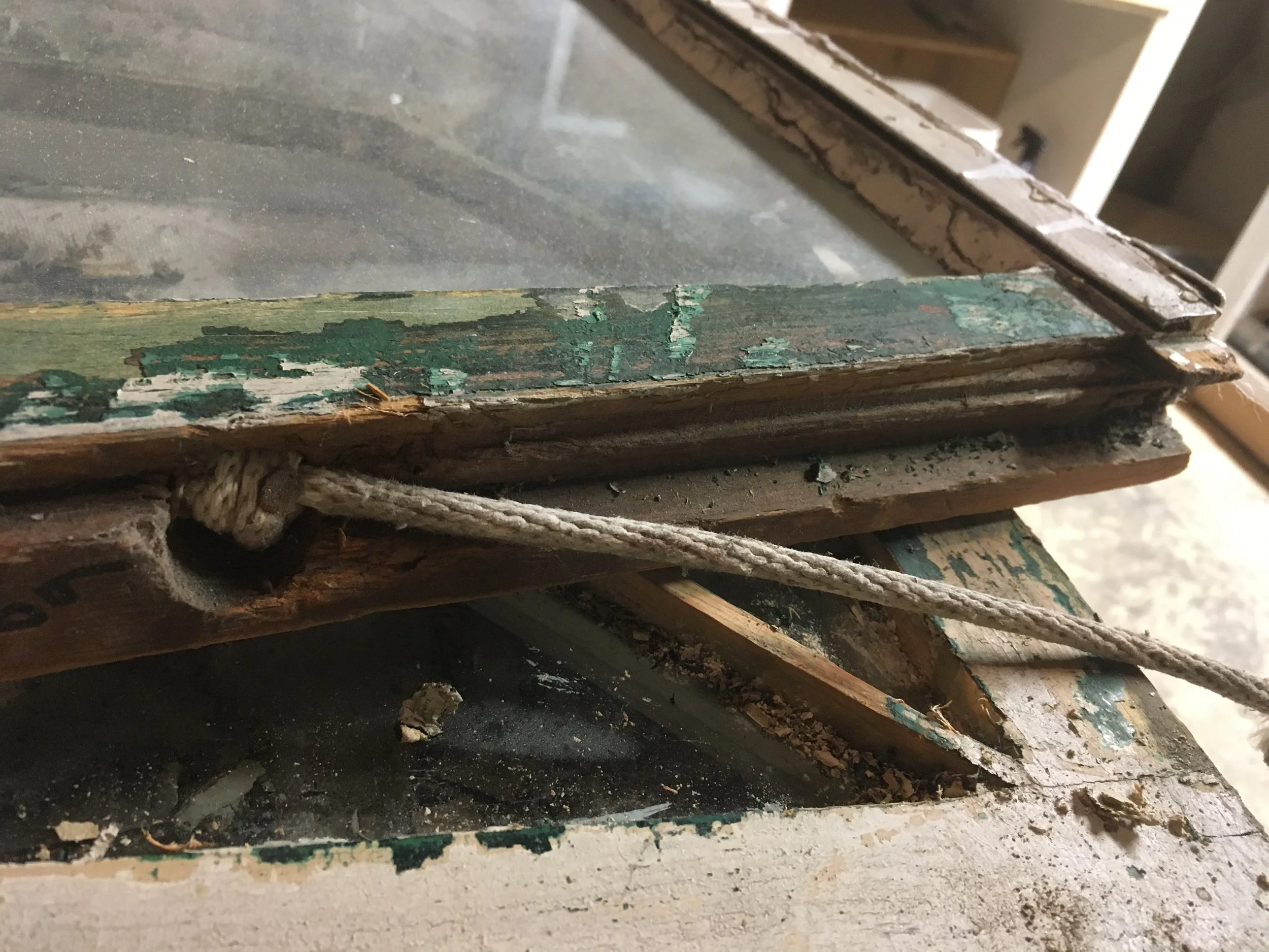 Close-up of a weathered, damaged window with peeling green paint and a frayed rope.