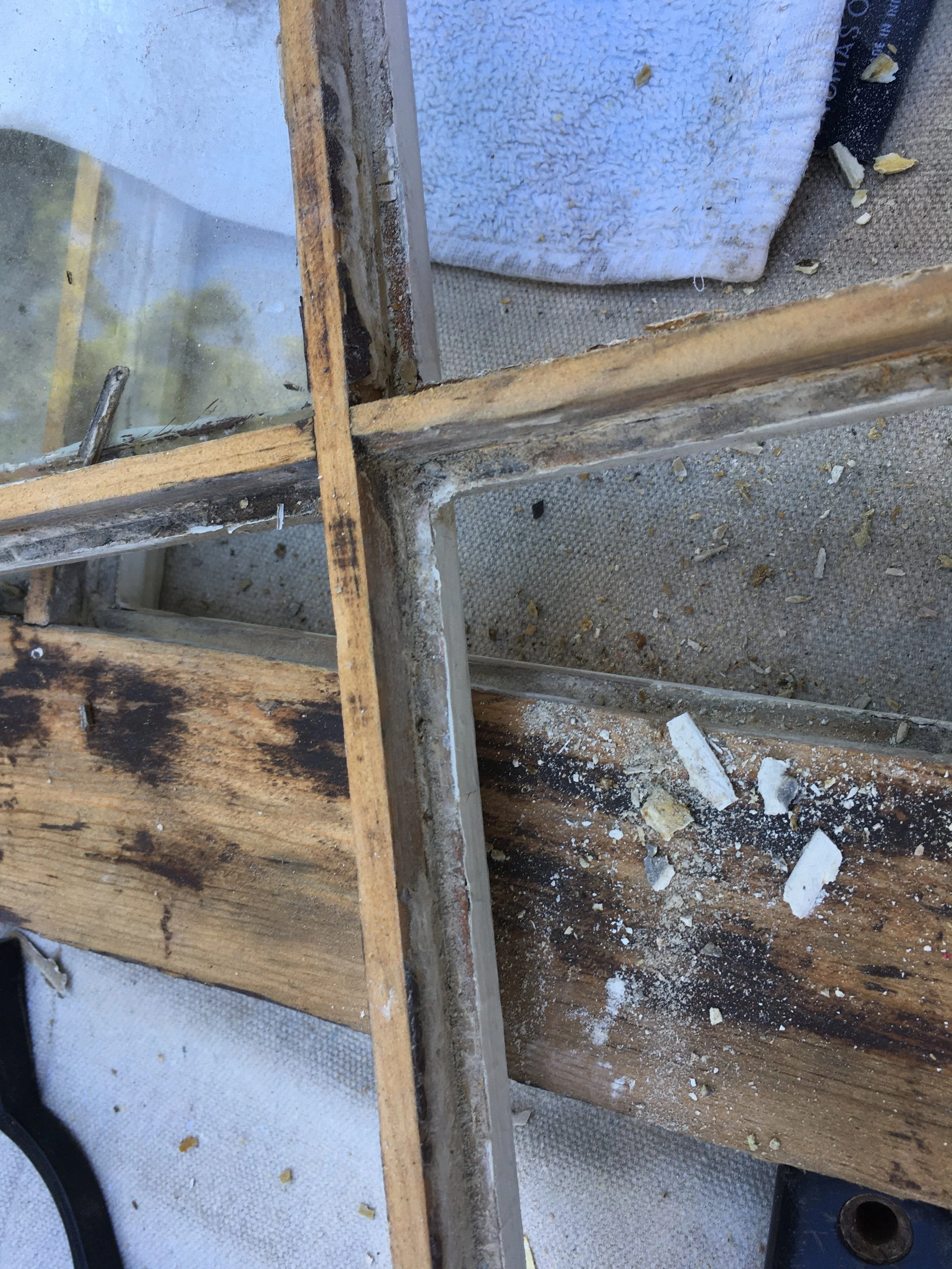 Close-up of a damaged wooden window frame with broken glass and debris, possibly during a renovation or repair.