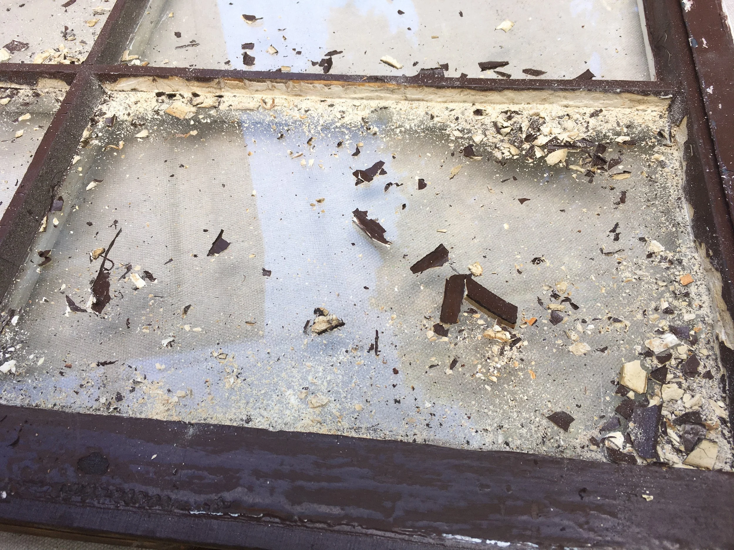 A shattered glass display case with dirt, debris, and broken pieces of glass inside.