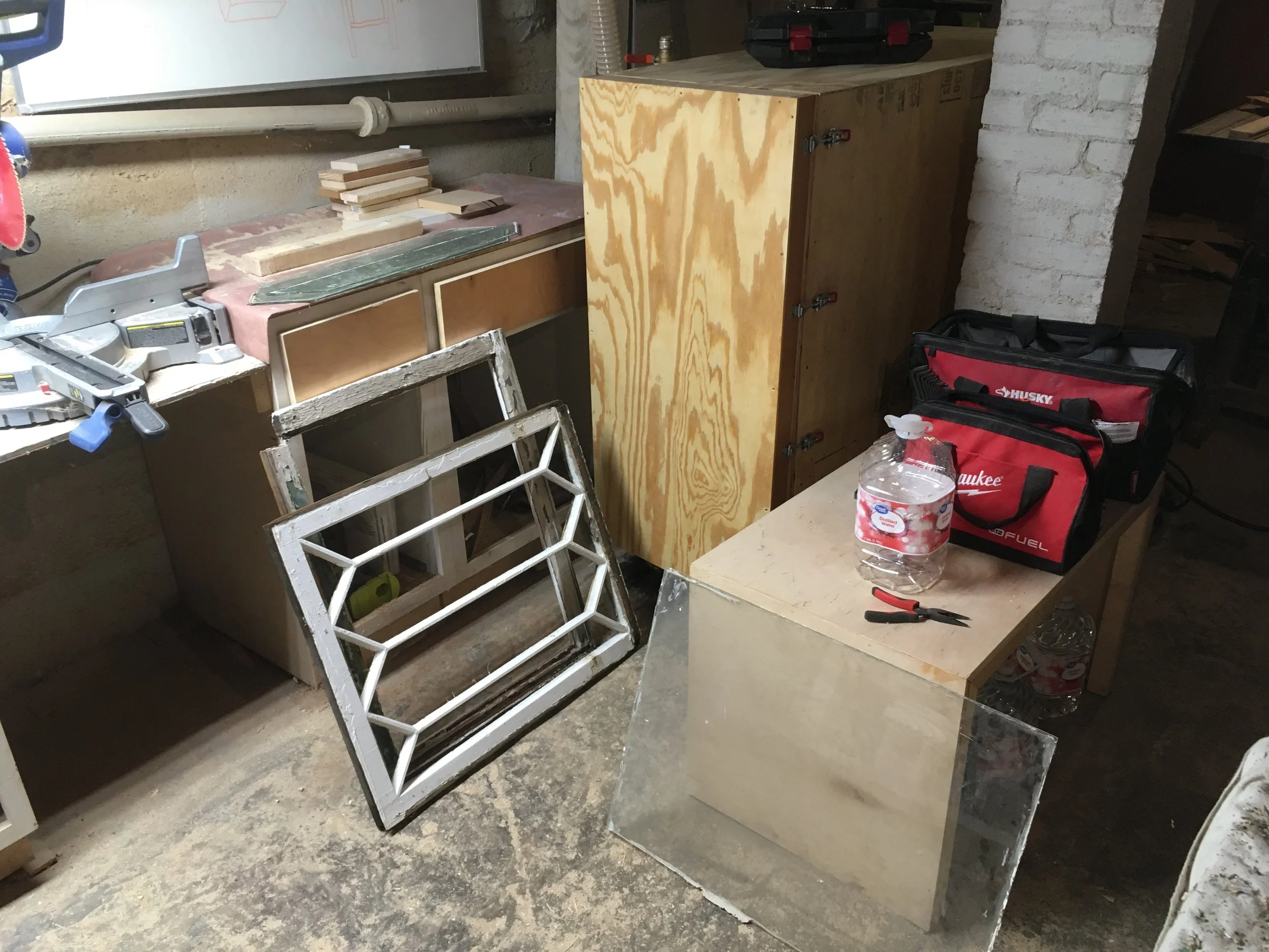 Workshop with woodworking tools, wooden cabinets, a metal grate, a water bottle, a toolbox, and hand tools on a table.