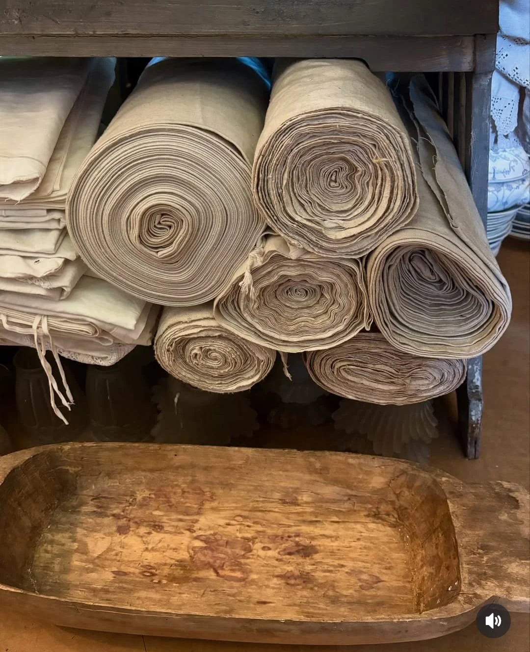 Multiple rolls of antique or vintage fabric stored on a shelf, with a wooden tray at the front.