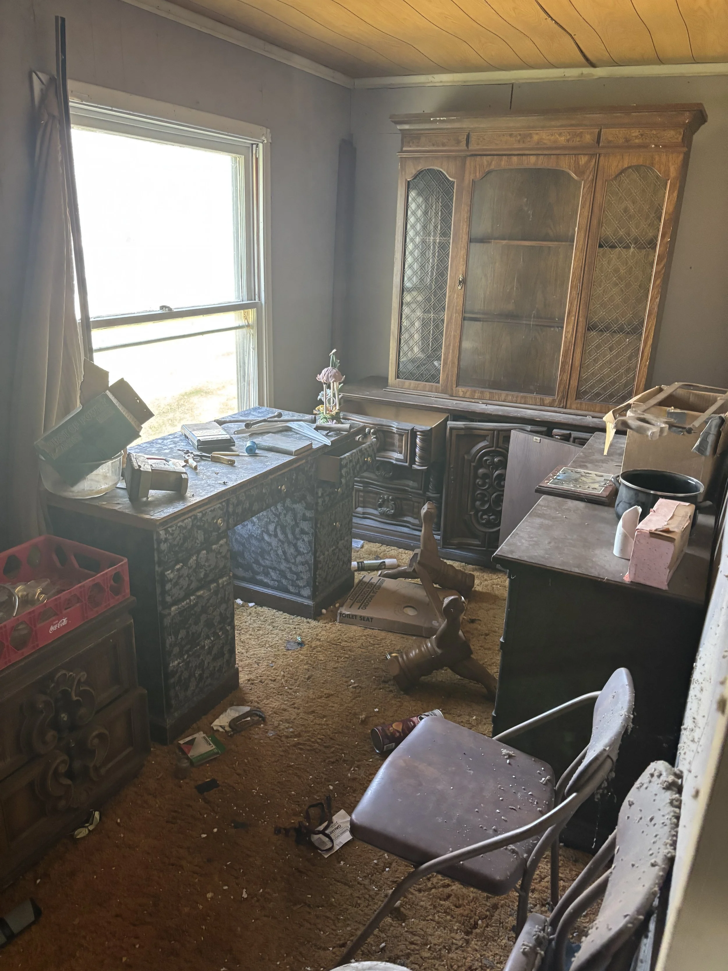 Cluttered, messy room with furniture, scattered items, and trash on the floor.