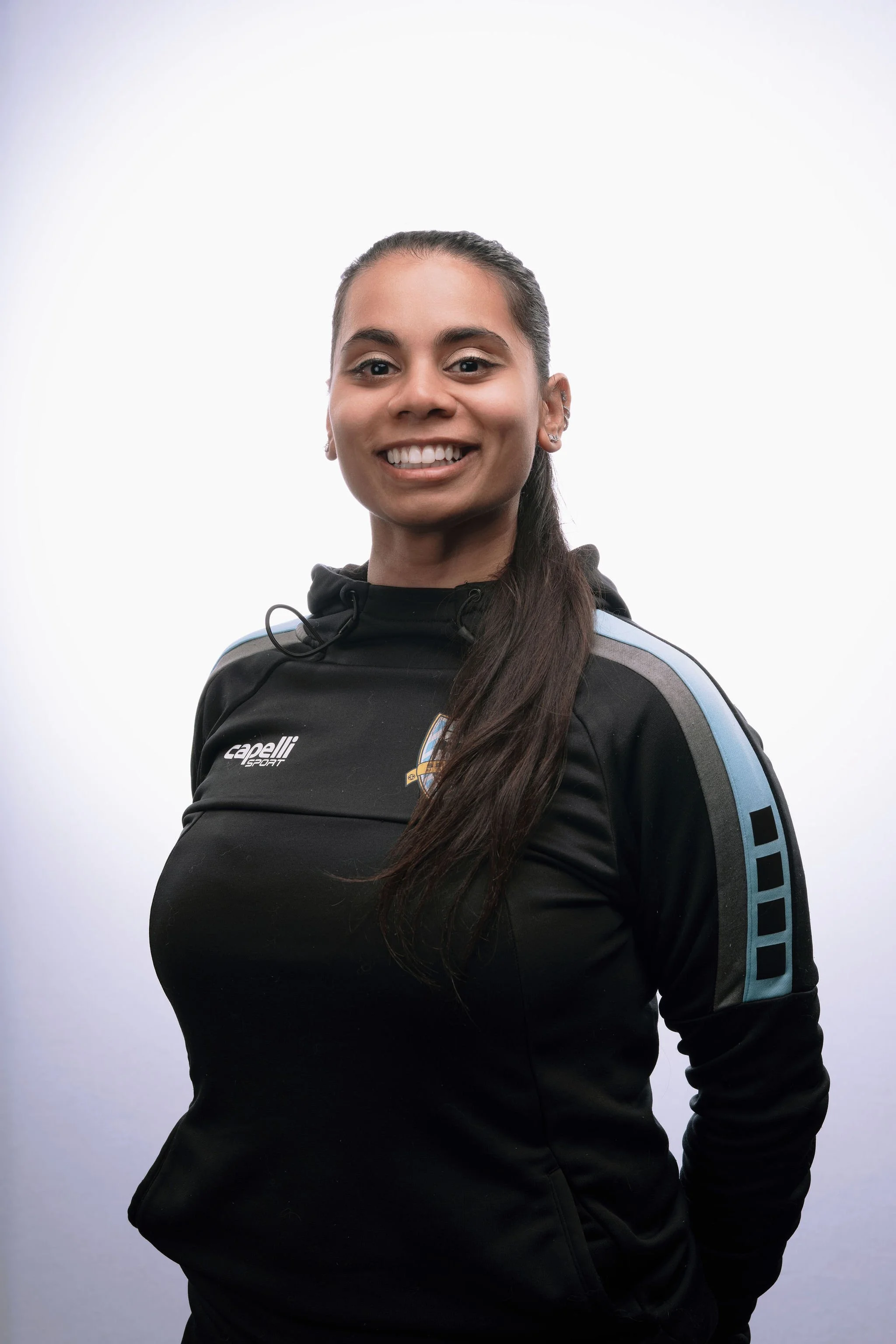 Young woman smiling, wearing a black sports jacket with blue and gray accents, against a plain white background.