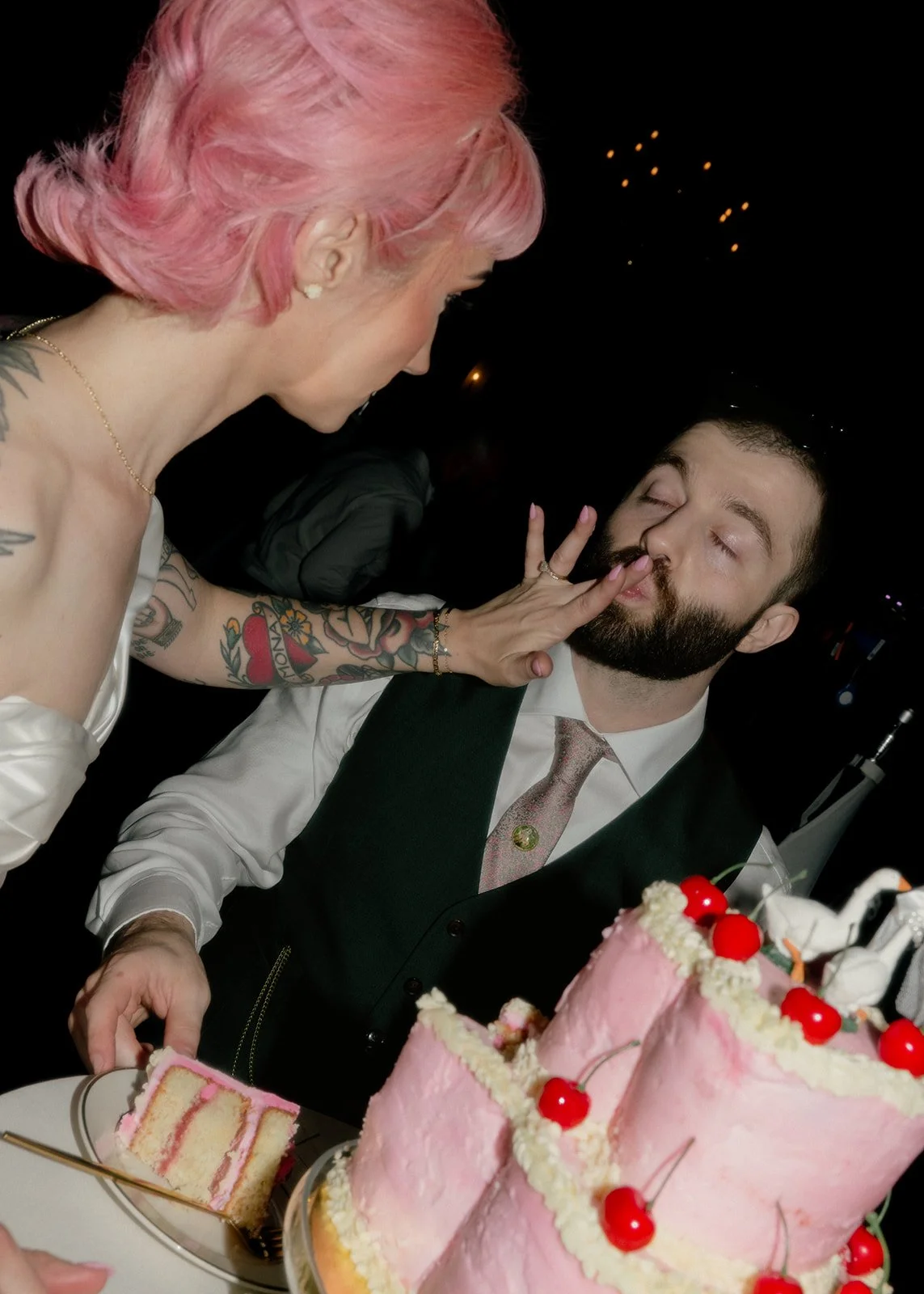 Tattooed bride feeds groom pink wedding cake on film