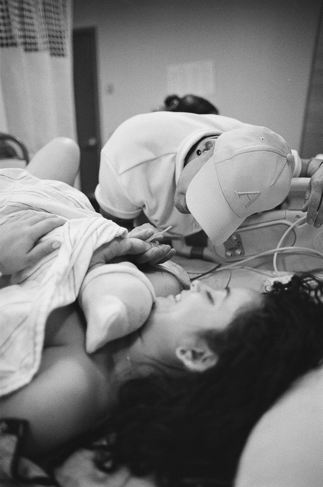 A woman lying in a hospital bed with a tube connected to her hand, a medical professional leaning over her, both in a hospital room.
