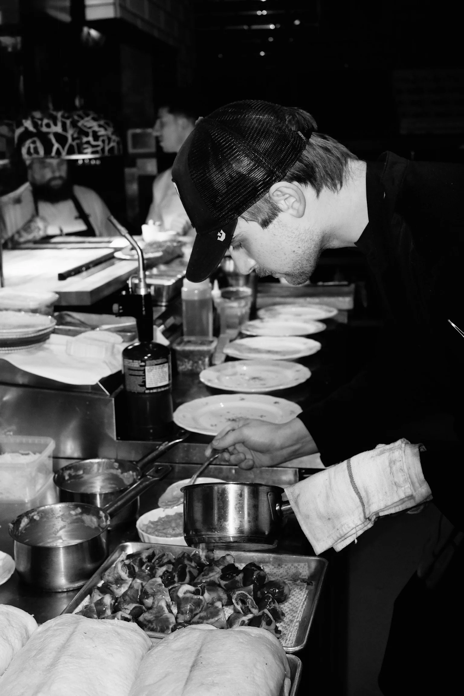 Un chef en train de préparer des plats dans une cuisine professionnelle, avec plusieurs assiettes et ingrédients sur le comptoir.