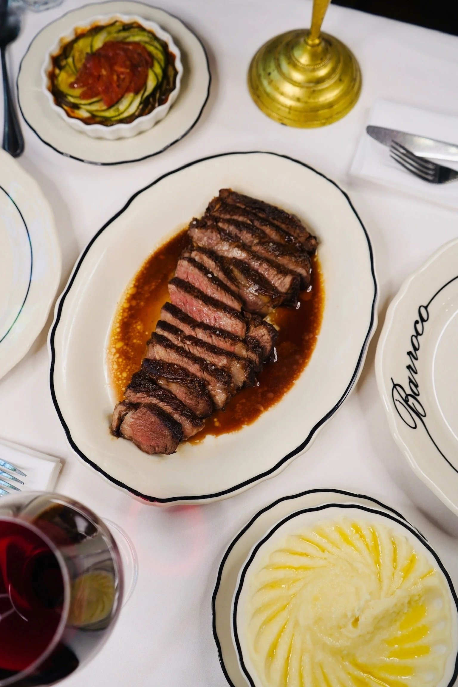 Plat principal avec steak coupé en tranches, accompagné de sauce, un plat de légumes en sauce, et un plat de purée de pommes de terre.