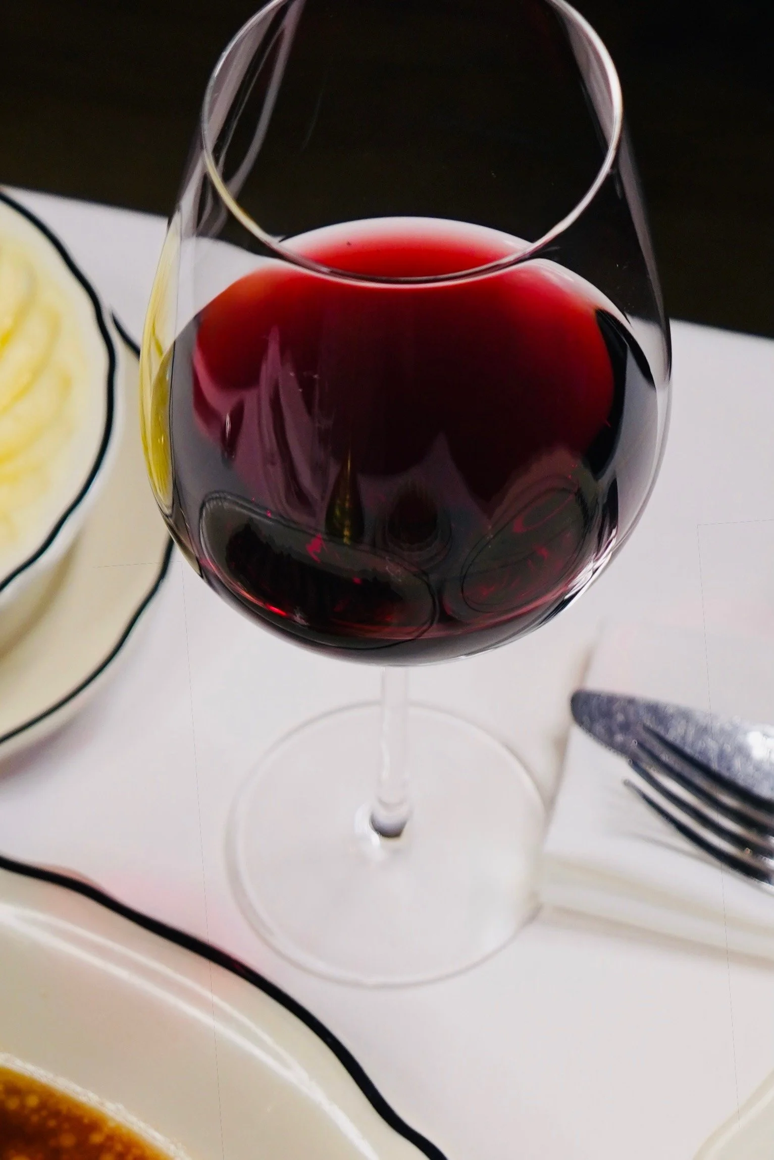 Verre de vin rouge sur une table avec assiettes et couverts.