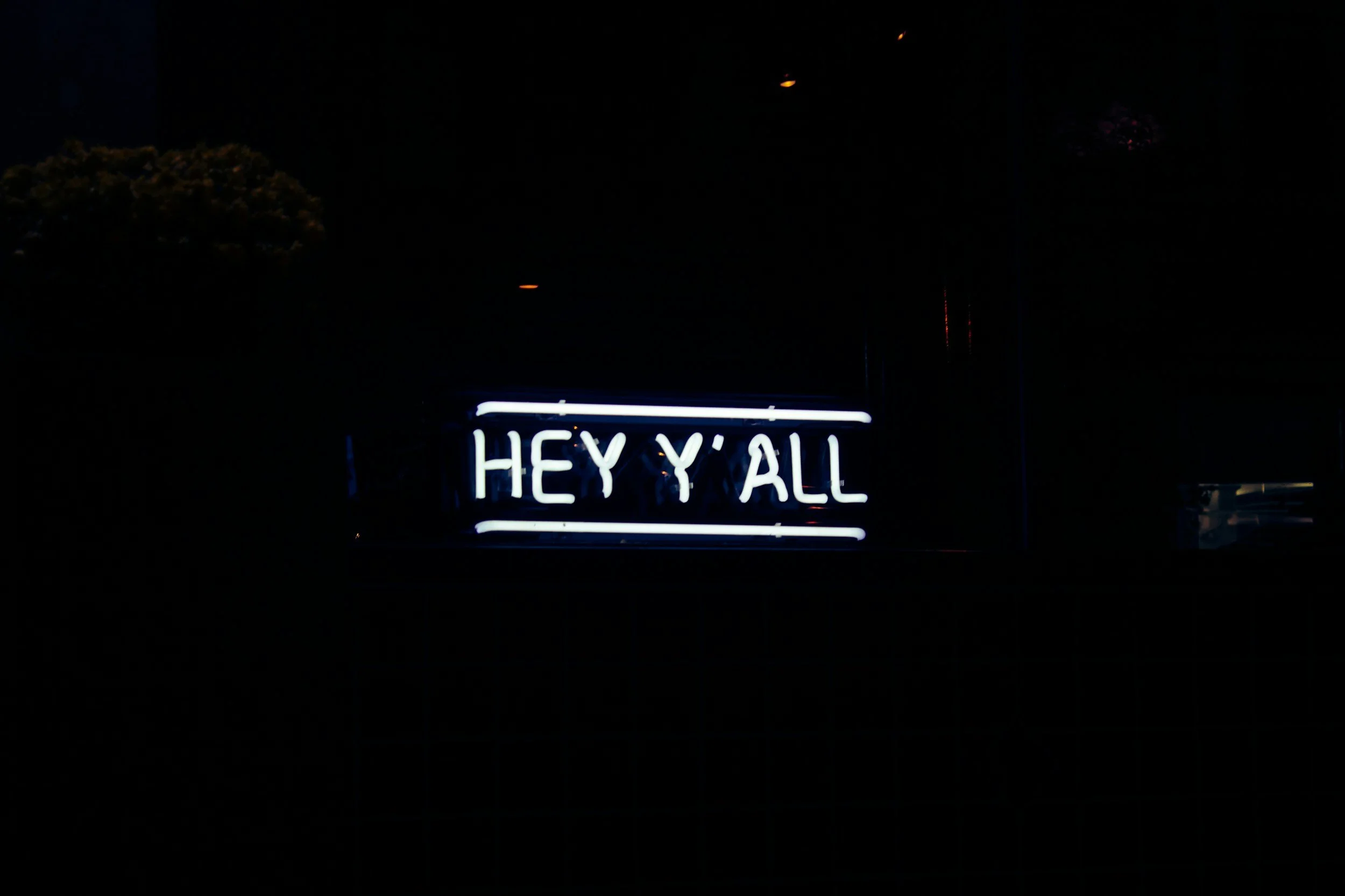 Neon sign displaying the message 'HEY Y'ALL' in capital letters, illuminated in white light against a dark background.
