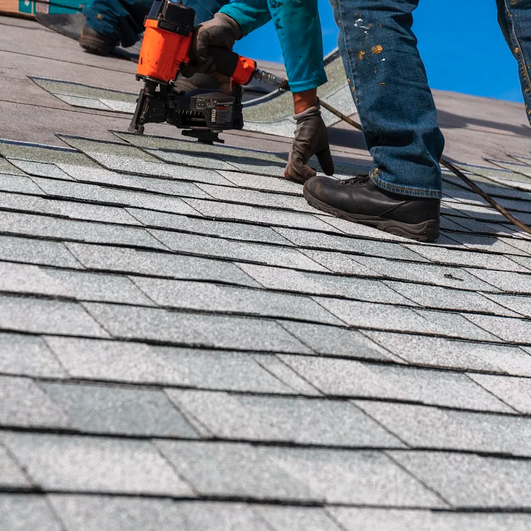 One worker bent over installing fire-proof roofing shingles
