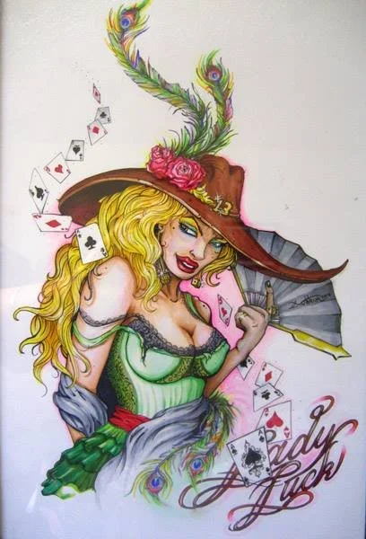 Colorful illustration of a woman with long blonde hair, wearing a green dress and a large wide-brimmed hat with feathers and pink flowers, surrounded by playing cards and the words 'Lady Luck' written in cursive.