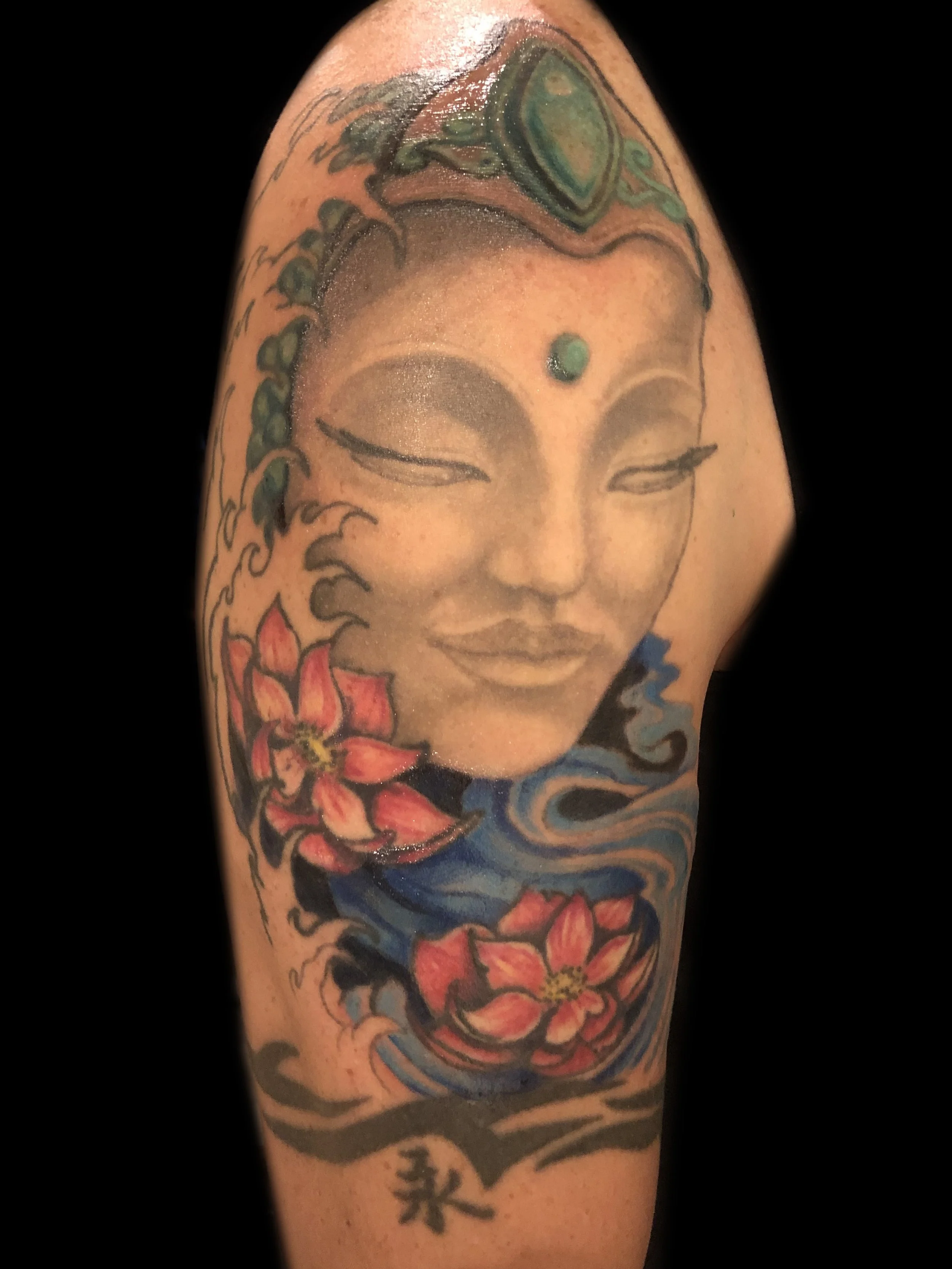 Tattoo of a serene face with closed eyes surrounded by red flowers and flowing water with blue and black swirls.