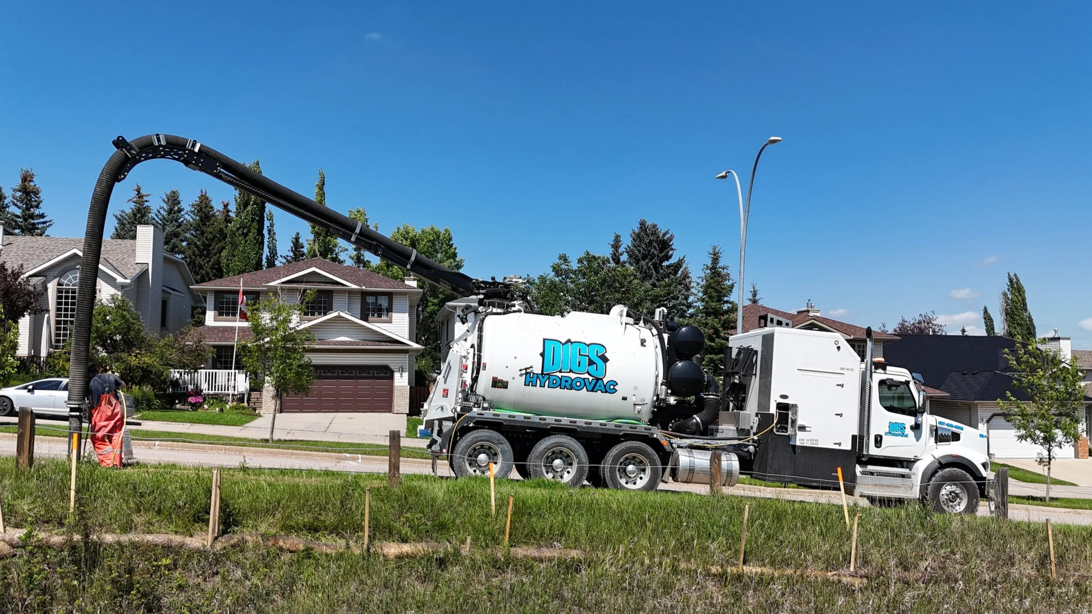 A HydroVac truck labeled 'Digs HydroVac' working on a residential street with houses and trees in the background.