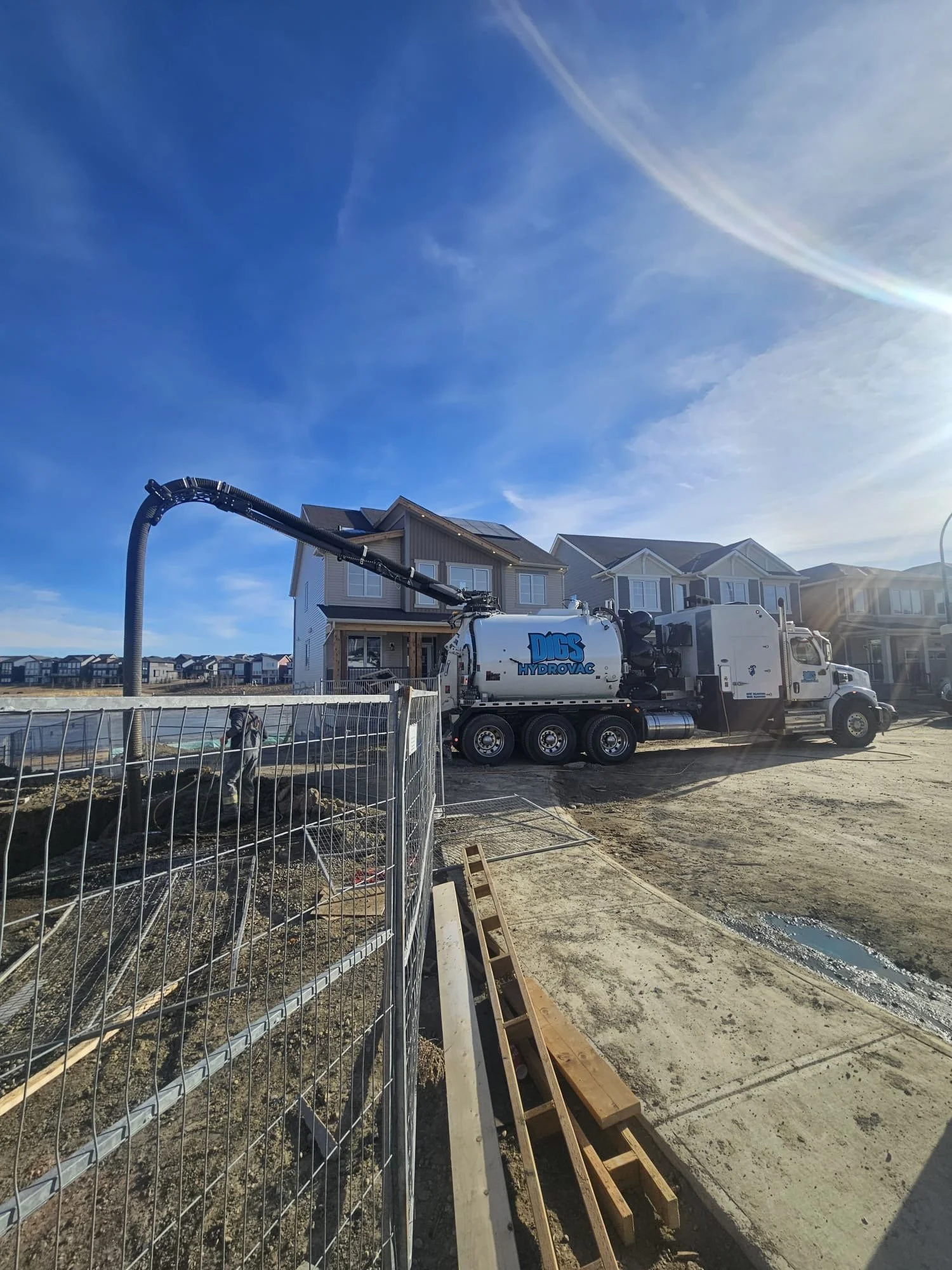 Construction site with a concrete pump truck pouring cement near a row of houses on a sunny day.