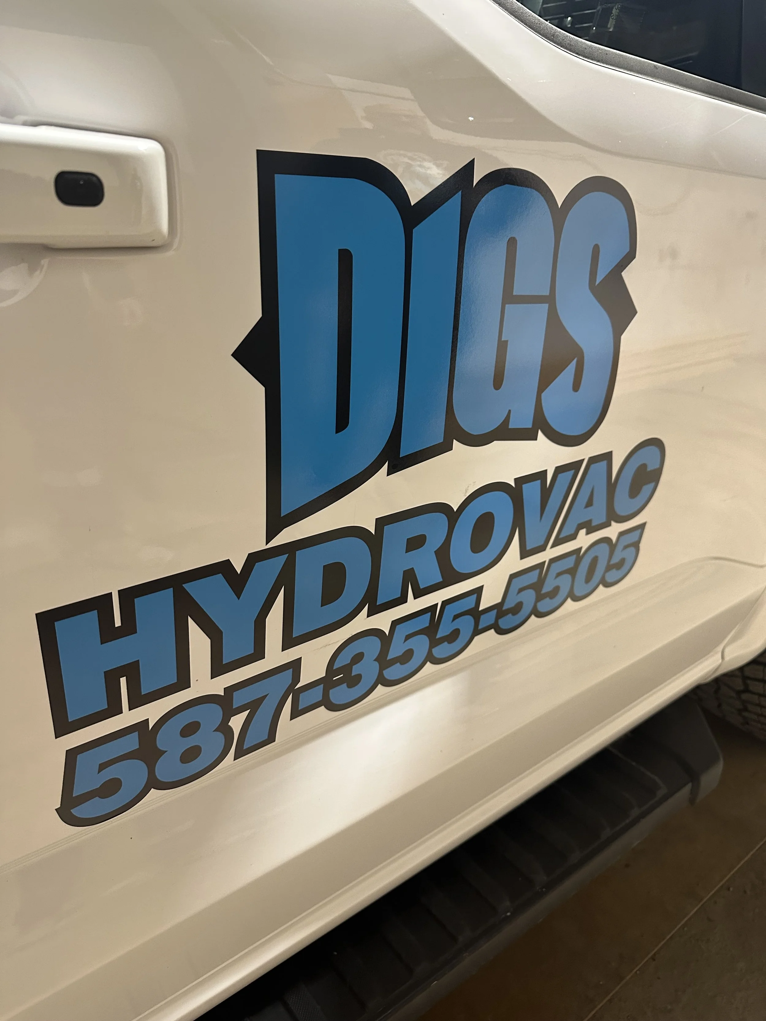 Close-up of a white vehicle with a sticker that reads 'Hydro-Force' in bold blue and black letters, along with a phone number in black.