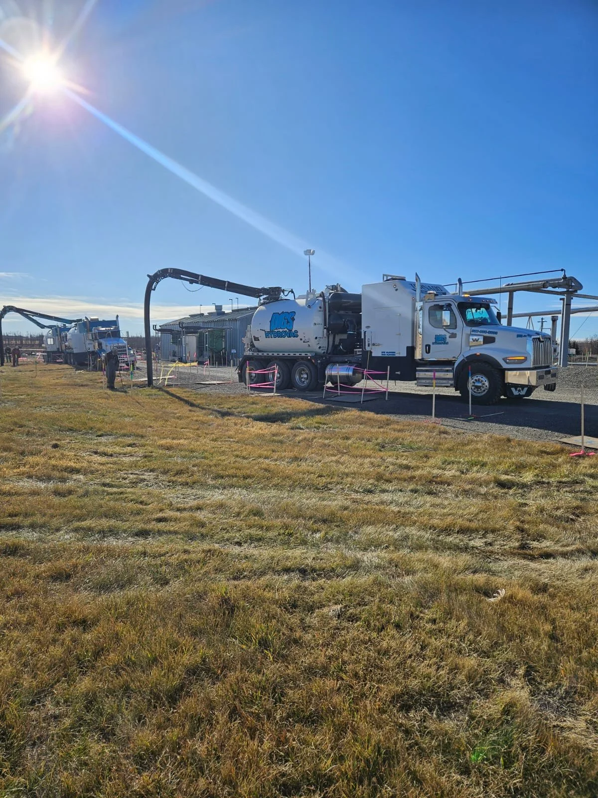 A water truck with industrial hoses set up outdoors on a dirt field on a bright, sunny day.