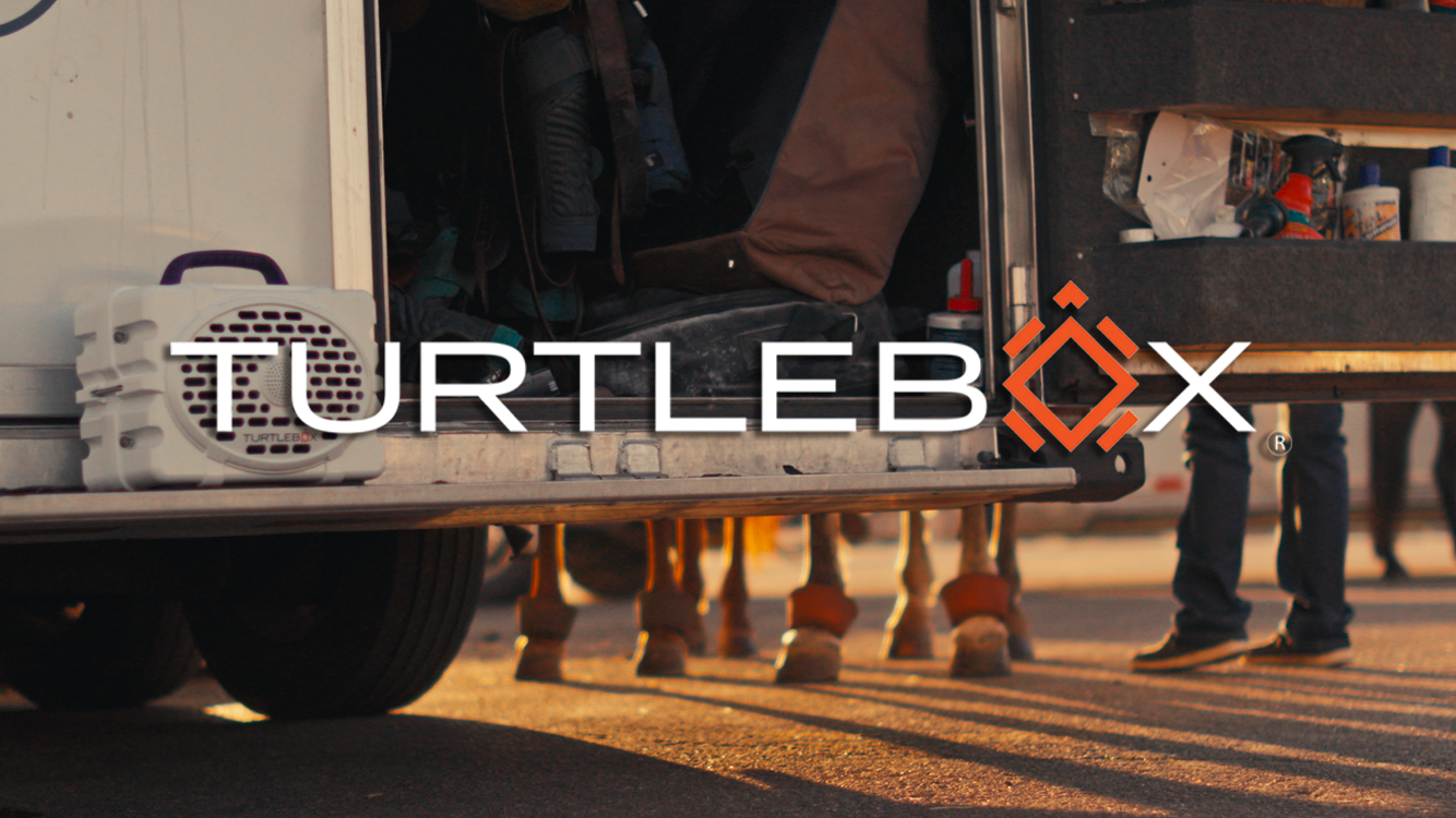 People and horses near a white trailer with an open door, with the logo 'TURTLEBOX' overlaid in the center.