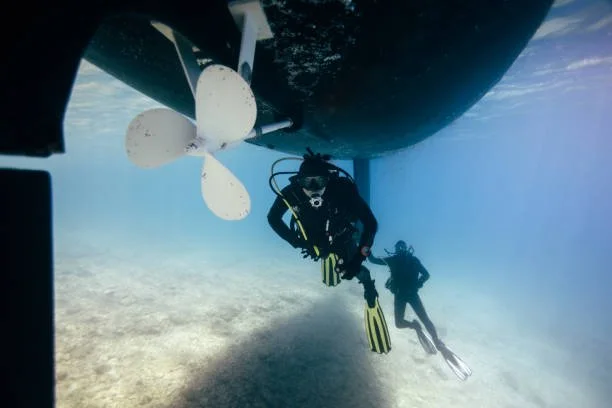 Two scuba divers exploring beneath a boat with a large white propeller.