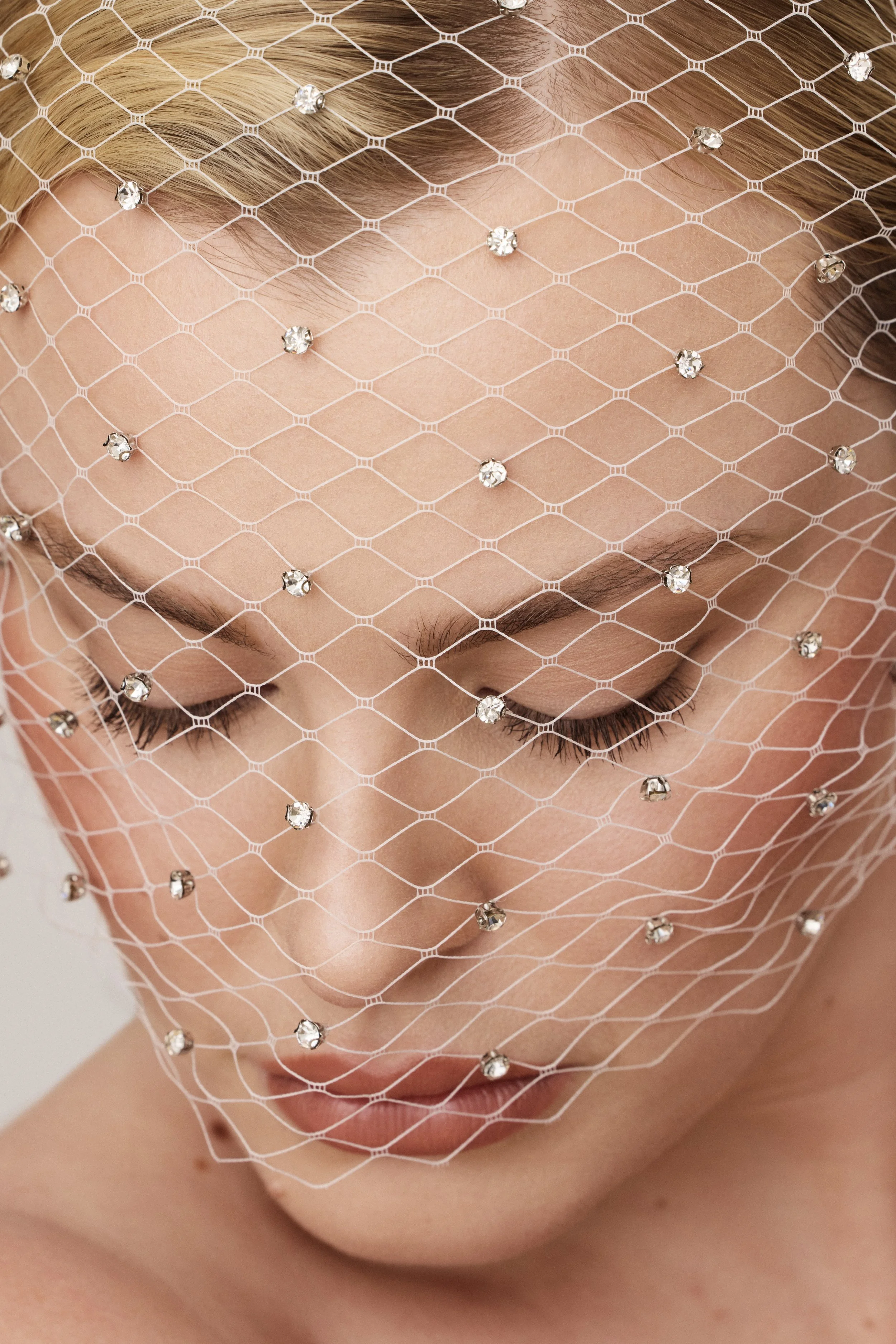 Modern bridal makeup with pearl accents and soft peach tones under a mesh veil – elegant editorial bridal beauty look.