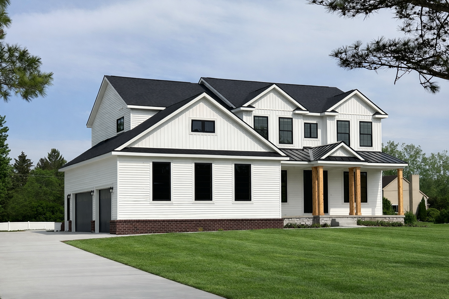A two-story house with white siding, black windows, and a black roof, featuring a front porch with wooden columns, a driveway, and a well-kept green lawn.