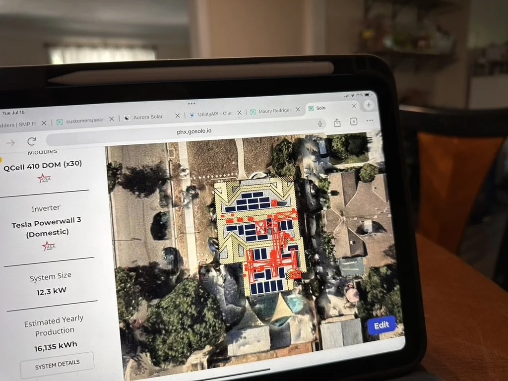 A tablet screen displaying a solar panel layout on a residential roof, with a map of the house and surrounding neighborhood.
