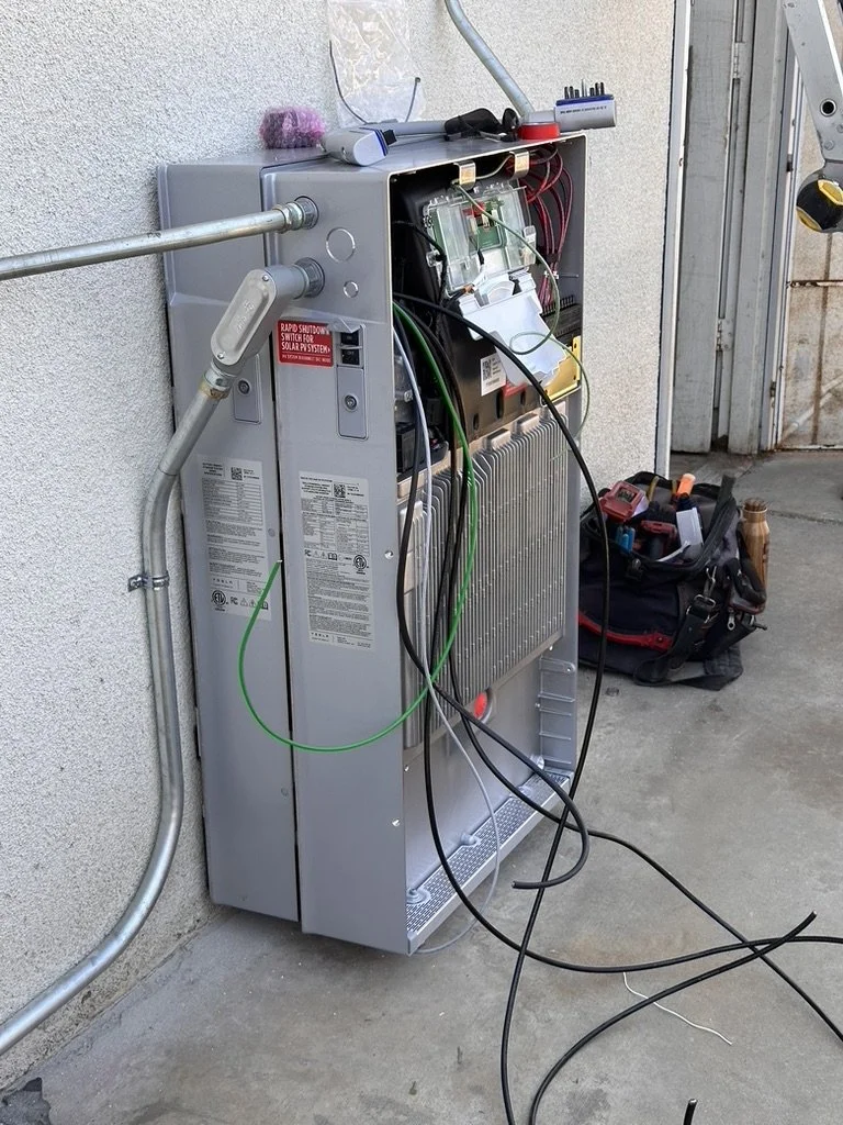 Outdoor utility box with exposed electrical components and wires, along with a tool bag on the ground nearby.