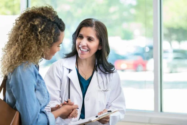 A female doctor and a woman patient smiling and talking in a medical office.
