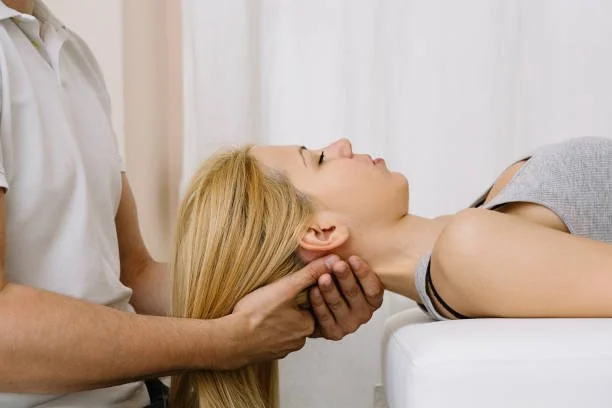 A woman receiving a chiropractic neck adjustment from a healthcare professional in a clinical setting.