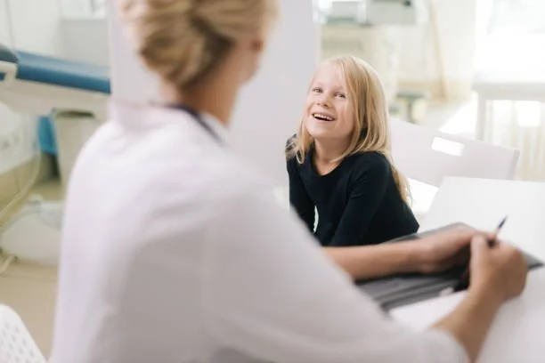 A young girl sitting in a medical office, smiling and talking to a healthcare professional.