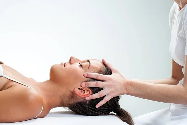 A woman receiving a head and neck massage from a therapist in a clinical setting.