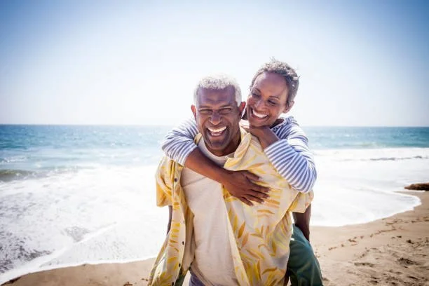 A joyful couple enjoying a piggyback ride on the beach with the ocean in the background.