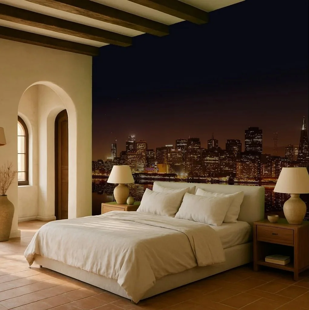 A bedroom with a large bed, white linens and pillows, two bedside tables with lamps, plush carpeting, and a large mural of a city skyline at night on the wall in the background.