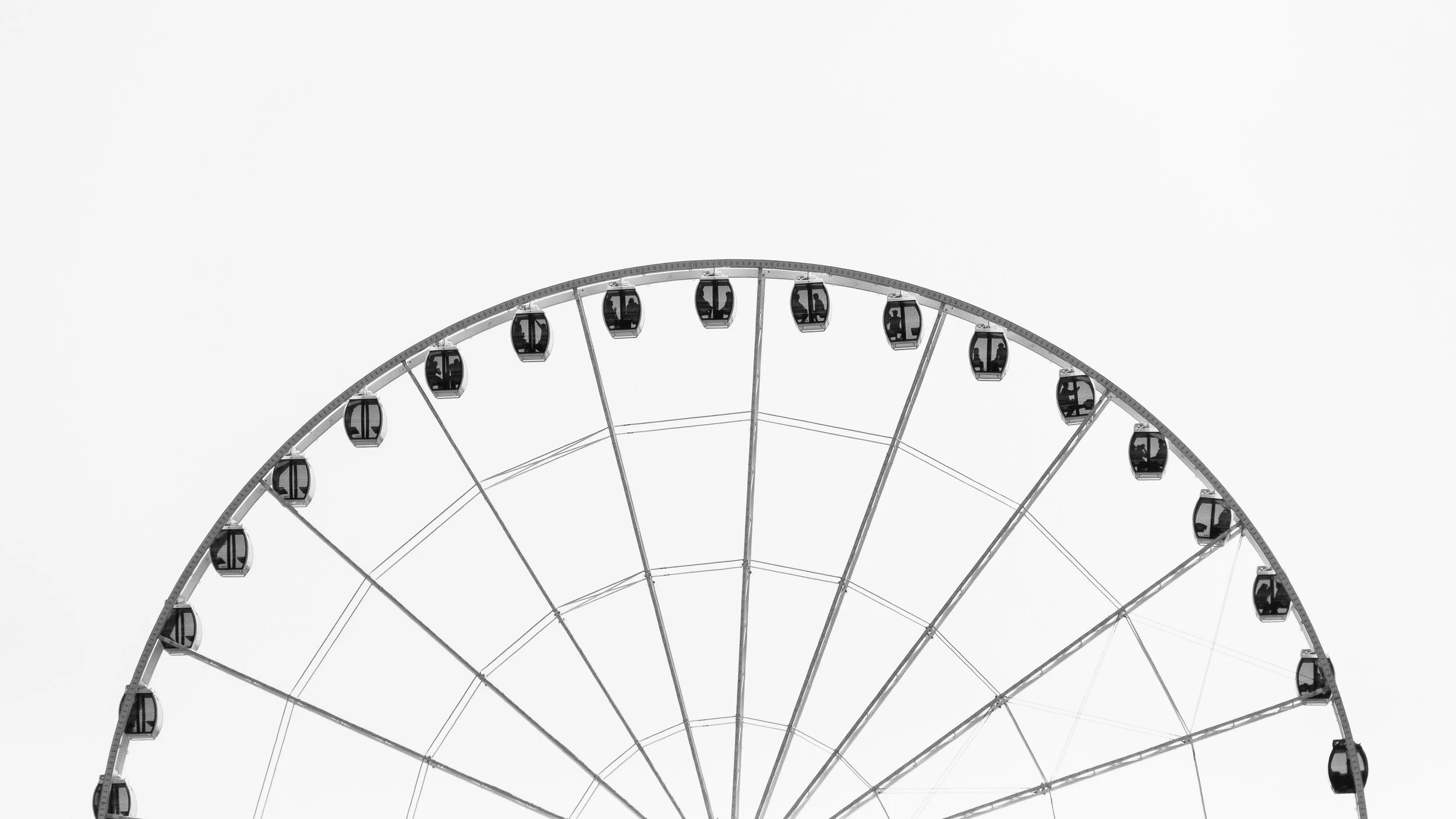 Close-up of a Ferris wheel with a white sky background.