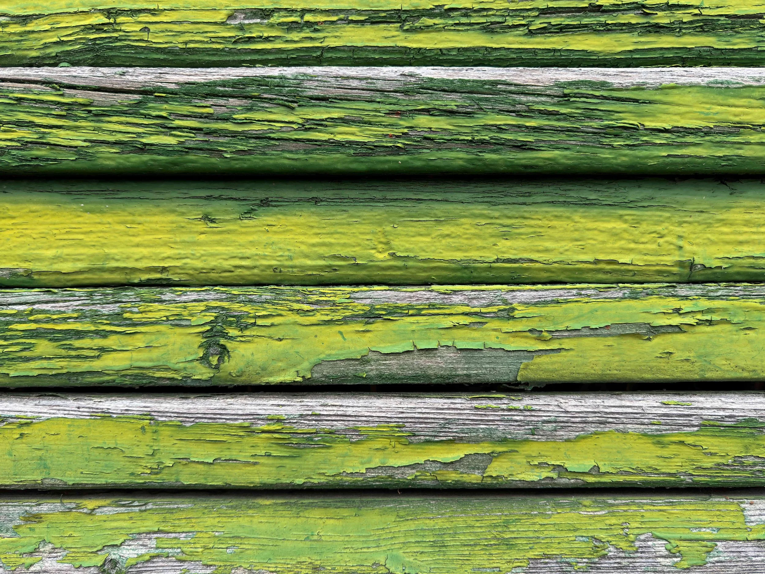 Close-up of weathered green painted wooden planks with peeling paint.